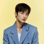 Retrato do ator e cantor sul-coreano Seo In-guk vestindo um terno azul claro de estilo elegante em um fundo amarelo.